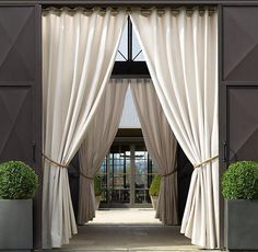 an open door with curtains and potted plants on either side, in front of it