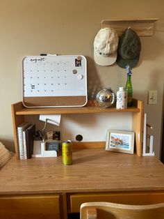 a wooden desk topped with a calendar and two hats hanging on the wall above it