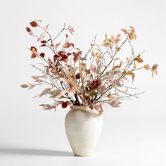 a white vase filled with lots of different types of flowers and leaves on a table