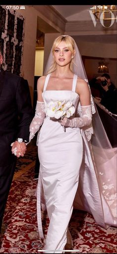 the bride and groom are walking down the aisle together in their wedding gowns, veils and gloves