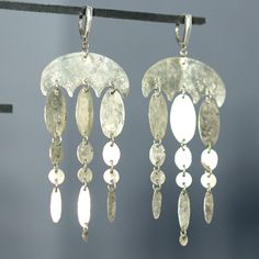 "Large, lightweight statement earrings with beautiful motion and sparkle. The central piece is a wide, hammered and textured, curved organic shape which hangs from a lever back earwire. Attached to the central piece are three chains of hammered and textured ovals with largest at the top and decreasing in size at the lower end. The central chain is slightly longer than the outer chains. All metal used in this is Fine or Sterling Silver. Dimensions: Width at widest point 1 1/2\" (38 mm), length from top of ear wire to bottom of earring 3 7/8\" (97 mm)." Sterling Silver Chandelier Dangle Earrings, Elegant Metal Chandelier Earrings With Lever Back, Fusion Style Sterling Silver Dangle Chandelier Earrings, Sterling Silver Fusion Chandelier Dangle Earrings, Silver Long Drop Chandelier Earrings In Brass, Modern Handmade Long Drop Chandelier Earrings, Long Drop Metal Chandelier Earrings With Ear Wire, Modern Silver Chandelier Earrings With Ear Wire, Long Drop Metal Chandelier Earrings