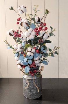 a vase filled with cotton and berries on top of a wooden table next to a wall