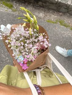 a person holding a bouquet of flowers in their hand on the street while another person walks by