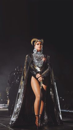 a woman in a costume on stage with a microphone and headpieces around her neck