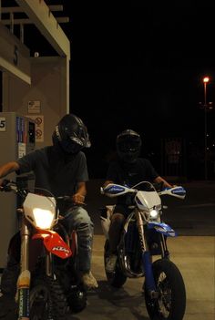 two people on motorbikes in front of a gas station at night with lights on