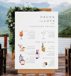 a sign with drinks on it sitting in front of a body of water that says, drunk is love signature drinks the bar menu