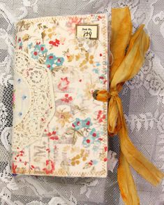 an old book with yellow ribbon on top of lace covered table cloth and white doily