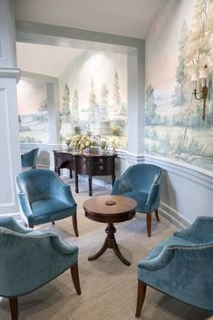 a living room filled with blue chairs next to a painting on the wall and a coffee table