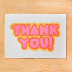 a thank card with the words thank you in pink and orange on a wooden surface