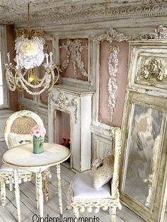 a white table and chair sitting in front of a fireplace with a chandelier hanging from it's ceiling