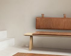 a brown bench sitting on top of a white floor next to a wooden table and stairs