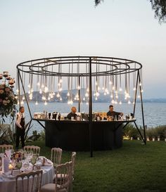 two people are sitting at an outdoor bar with lights hanging from the roof and chairs around it