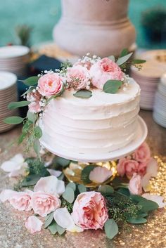 a white wedding cake with pink flowers and greenery on the top is sitting on a table