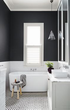 a white bath tub sitting under a bathroom window next to a sink and shower stall