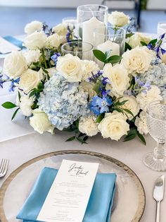 the table is set with blue and white flowers, silverware, and napkins