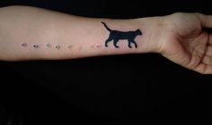 a person's arm with a small tattoo of a cat and paw prints on it