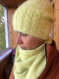 a man wearing a yellow hat and scarf next to a window with trees in the background