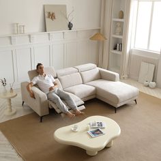 a man sitting on a couch in a living room next to a white coffee table