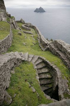 stairs lead down to the ocean from an old stone wall with moss growing on it