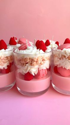 four desserts with strawberries and marshmallows in small glass containers on a pink surface