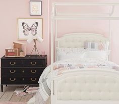 a white bed sitting next to a dresser in a pink room with pictures on the wall