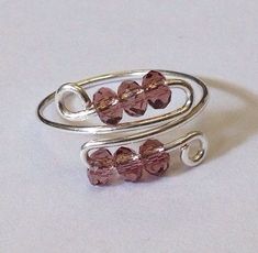 two silver rings with pink glass beads on them sitting on a white surface, next to each other