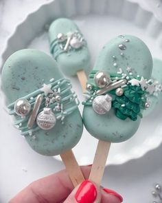 there is a hand holding two blue cake pops with decorations on them and one has a red manicure