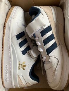 a pair of white and blue adidas sneakers in a cardboard box on the floor