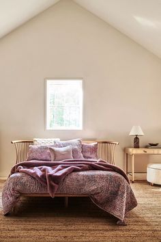 a bed sitting under a window in a bedroom next to a dresser and chair on top of a rug