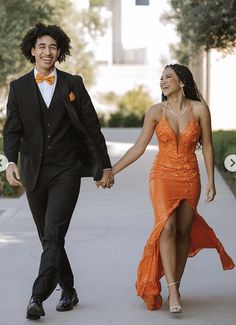 a man and woman dressed in formal wear walking down the street holding hands with each other