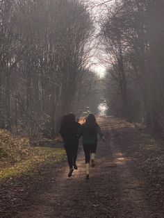 two people walking down a dirt road in the woods