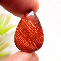 a close up of a person's hand holding a red and black tear shaped stone