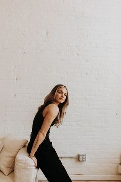 a woman sitting on top of a couch next to a white brick wall in a living room