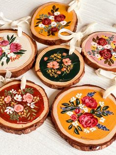 four wooden slices with flowers painted on them and tied in white ribbon around the edges