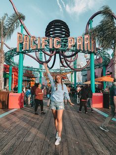 a woman walking under a sign that says pacific bar on the side of a boardwalk