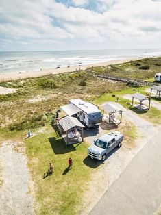 an rv park on the beach with people and vehicles parked in front of it next to the ocean