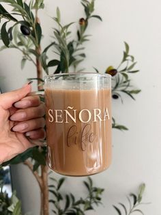 someone holding up a coffee mug with the word senioria on it in front of a plant