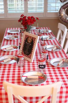 a red and white checkered table cloth with silver plates on it is set for a formal dinner