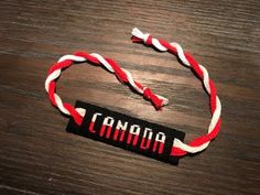 a red, white and black bracelet with the word canada on it sitting on top of a wooden table