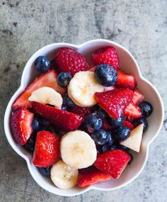 a white bowl filled with fruit on top of a gray counter next to a fork and knife