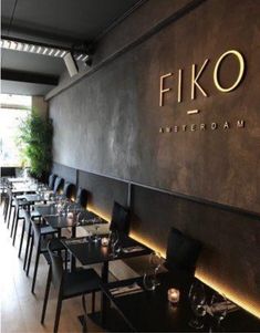 the interior of a restaurant with black tables and chairs in front of a large wall