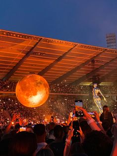 the crowd is taking pictures with their cell phones at an outdoor music concert in front of a giant orange ball