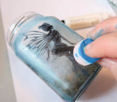 a person is painting on a glass jar with blue and white paint, next to some other items