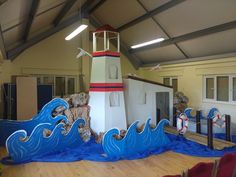 an indoor play area with fake waves and a lighthouse in the center, surrounded by wooden flooring