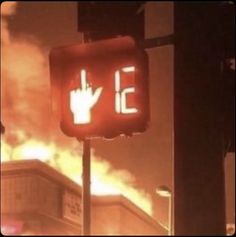 a fire blazing behind a building with a hand signal on it's red light