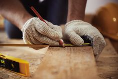 a person with gloves on writing on a piece of wood next to a tape measure