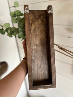 a person holding a plant in a wooden box with metal brackets on the top and bottom