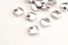 small silver heart shaped charms on a white surface with clippings to the side