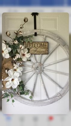 a welcome sign hanging on the front door of a house with white flowers and greenery