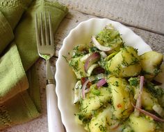 a white plate topped with potato salad next to a fork and green napkin on top of a wooden table